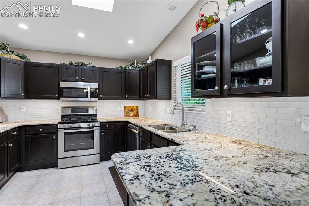 Image 9 of 44: Kitchen with stainless steel appliances, light stone counters, backsplash, 