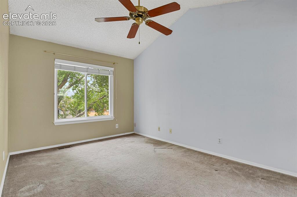 Image 13 of 48: Room featuring a vaulted ceiling with a ceiling fan, a large window, and wa
