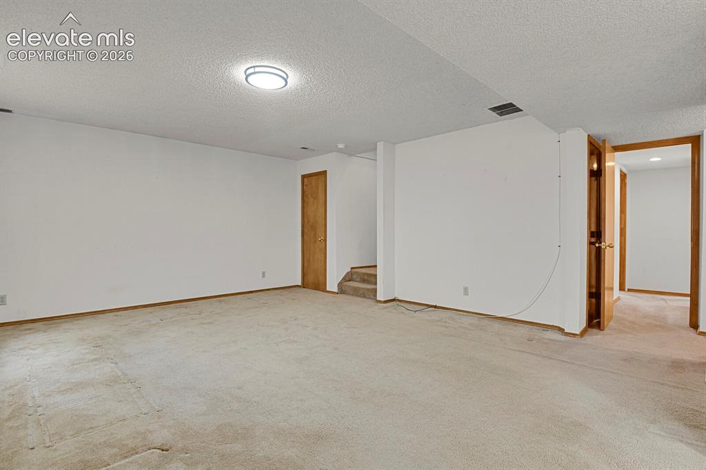 Image 34 of 48: Spacious lower-level room featuring light-toned carpeting and neutral wall 
