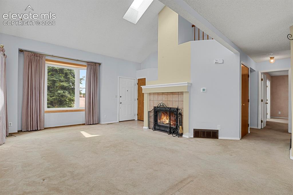 Image 35 of 48: Living area featuring a vaulted ceiling with skylight, a large window, a fi