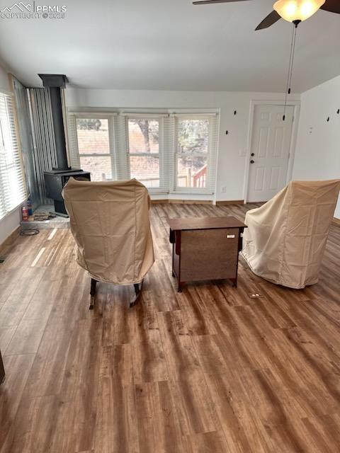 Image 17 of 23: Living area with wood finished floors, a wood stove, and a ceiling fan