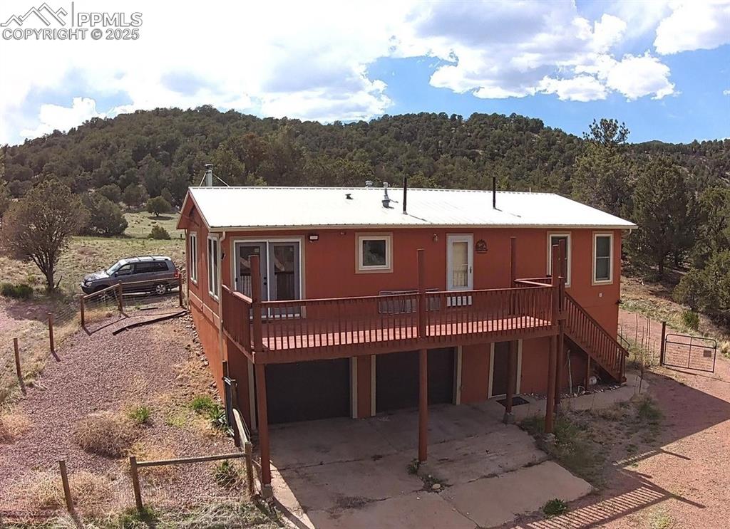 Image 3 of 23: Rear view of house featuring a view of trees, a deck, stairs, and concrete