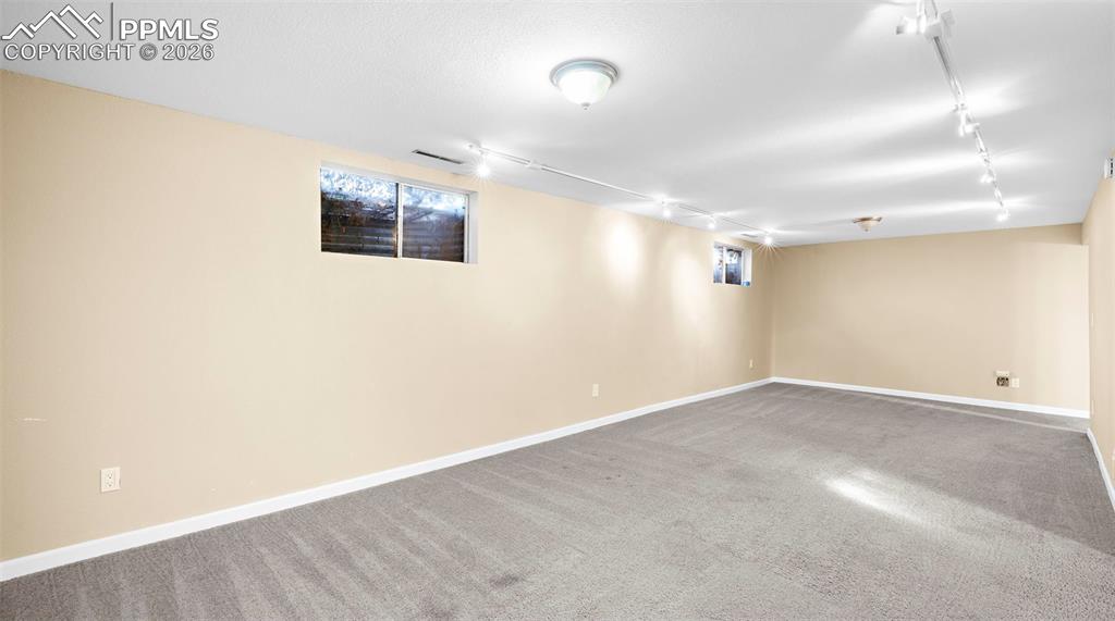 Image 21 of 32: Basement with rail lighting and carpet floors