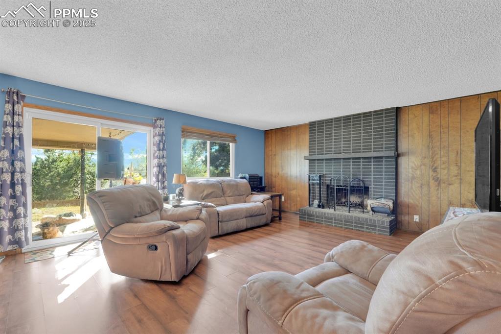Image 18 of 32: Living area with wooden walls, a tile fireplace, a textured ceiling, and wo
