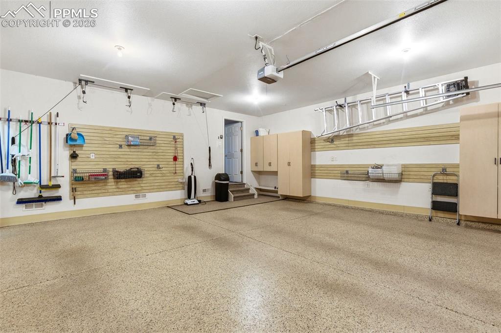 Image 28 of 40: Spacious garage featuring a speckled epoxy floor coating, built-in cabinetr