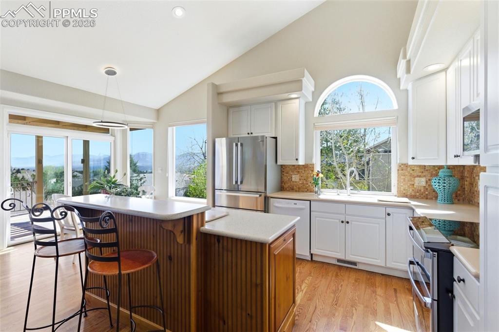 Image 4 of 40: Vaulted ceiling kitchen featuring white cabinetry, light countertops, wood-