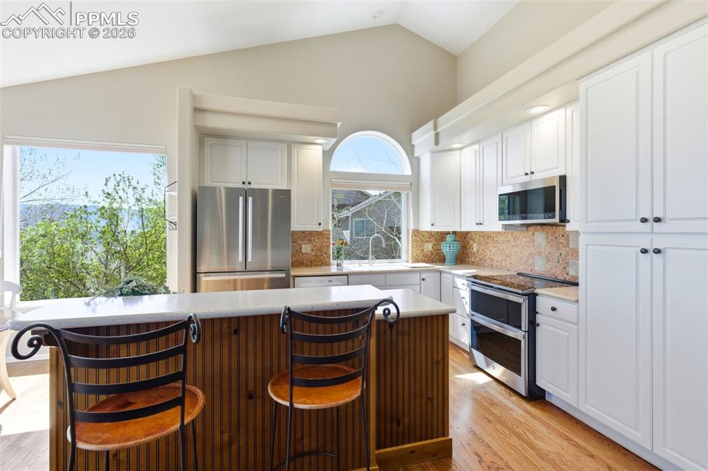 Image 5 of 40: Vaulted ceiling kitchen featuring white cabinetry, stainless steel applianc