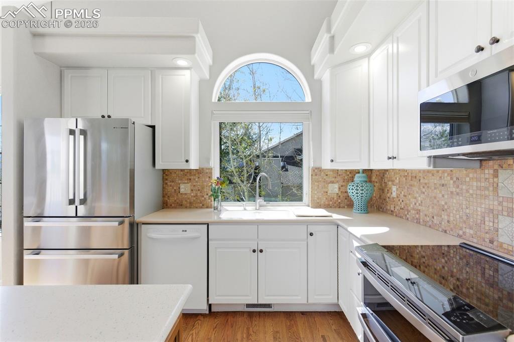 Image 9 of 40: Bright kitchen with white cabinetry, stainless steel appliances, a tile bac