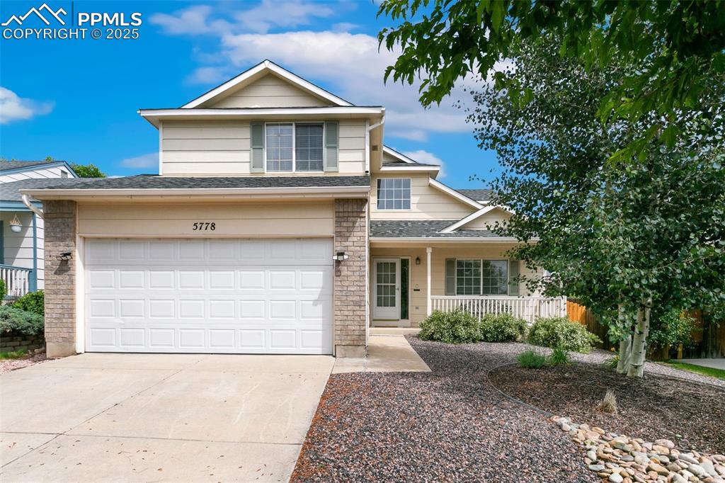 Caption: Traditional-style house featuring a porch, driveway, a shingled roof, and a garage