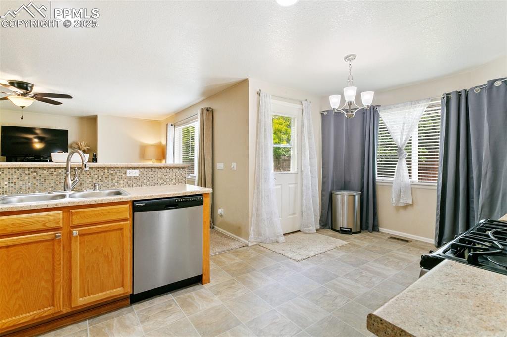 Image 12 of 46: Kitchen with stainless steel dishwasher, tasteful backsplash, a chandelier,