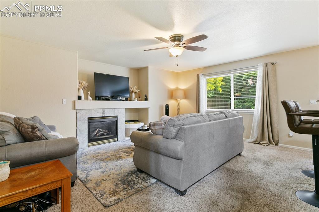 Image 17 of 46: Carpeted living room with ceiling fan and a tile fireplace
