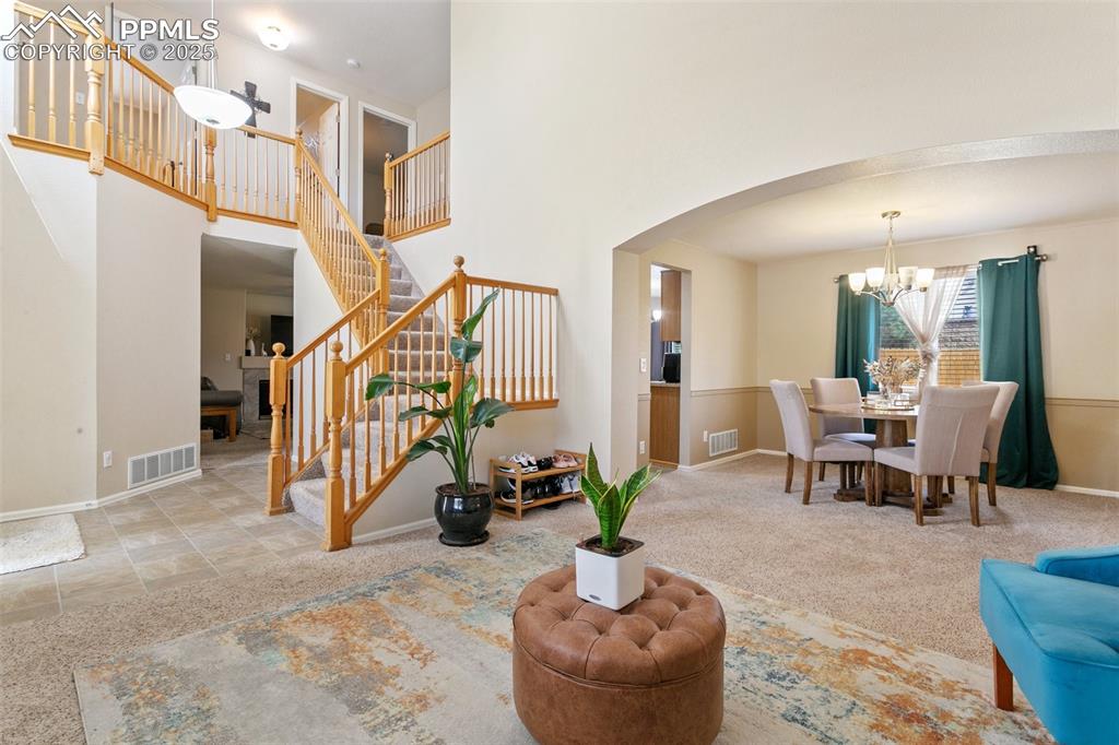 Image 5 of 46: Carpeted living area with arched walkways, a chandelier, a towering ceiling