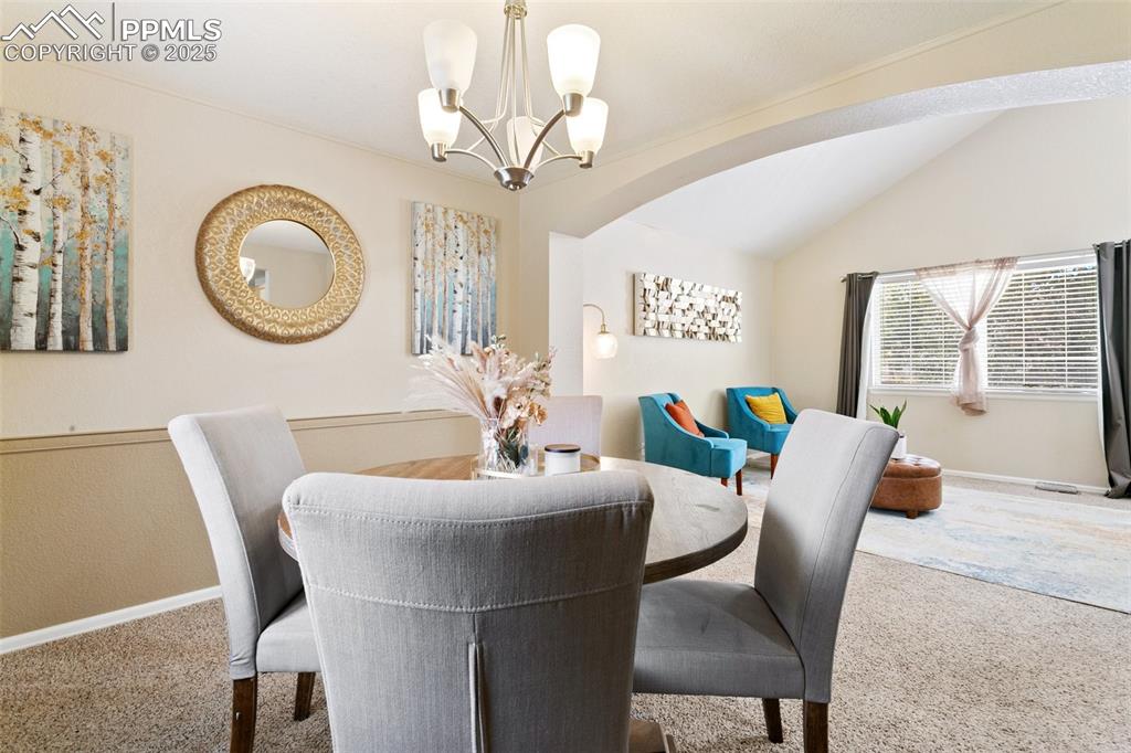 Image 9 of 46: Carpeted dining area with a chandelier and vaulted ceiling