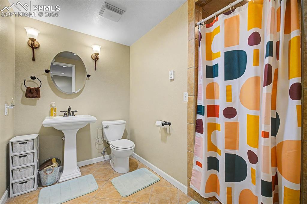 Image 30 of 49: The basement bathroom features a pedestal sink, a round mirror, and a color