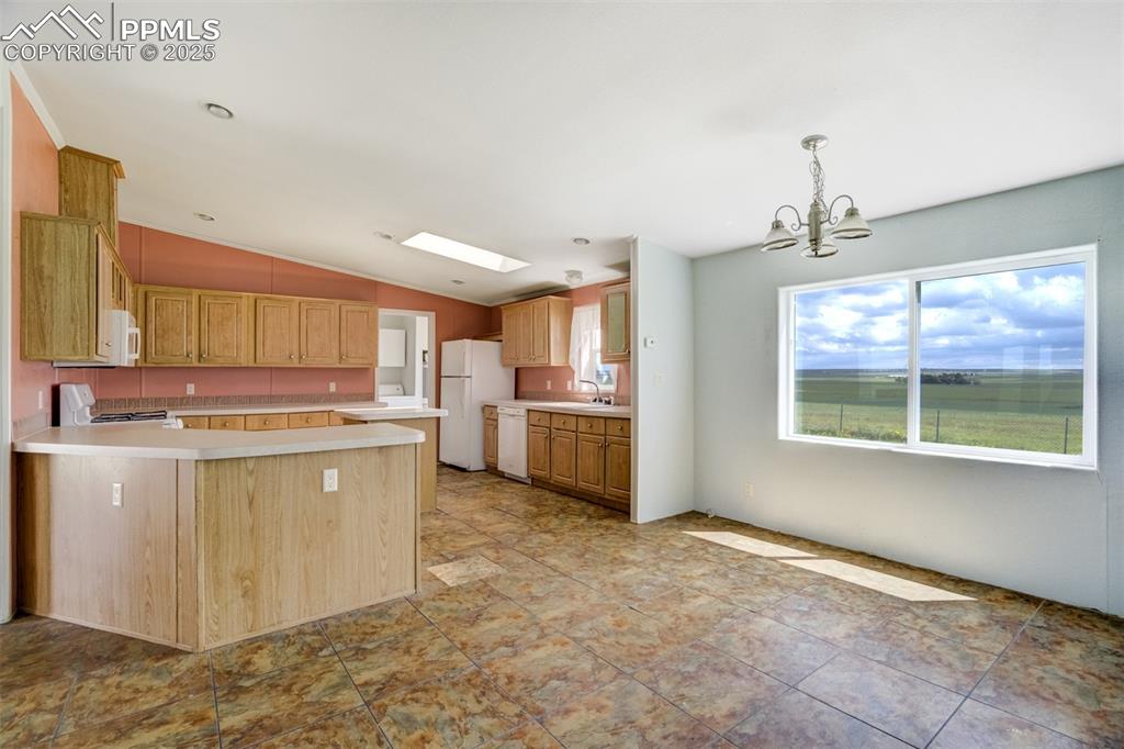 Image 13 of 49: Kitchen with white appliances, vaulted ceiling, a chandelier, light counter