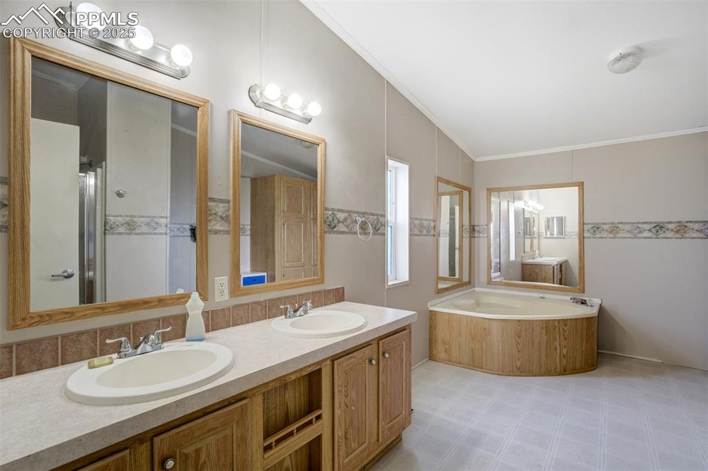 Image 22 of 49: Bathroom featuring double vanity, a bath, crown molding, and a shower with 