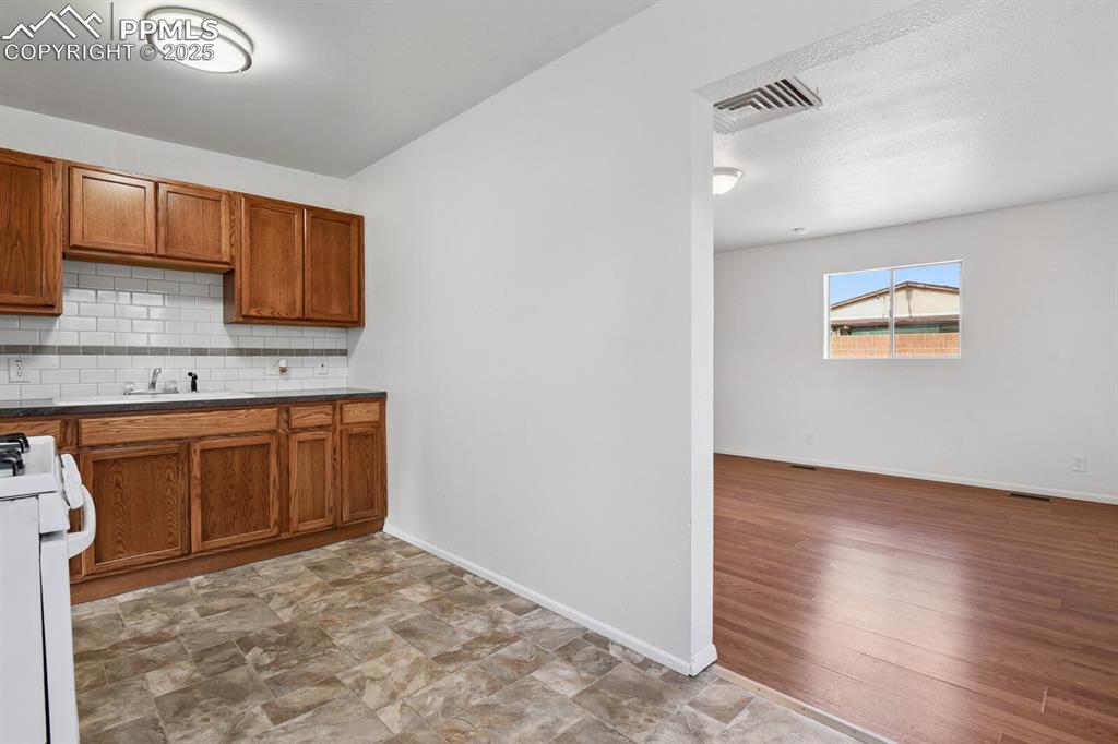 Image 11 of 33: Kitchen with backsplash, white gas range, brown cabinets, stone finish floo