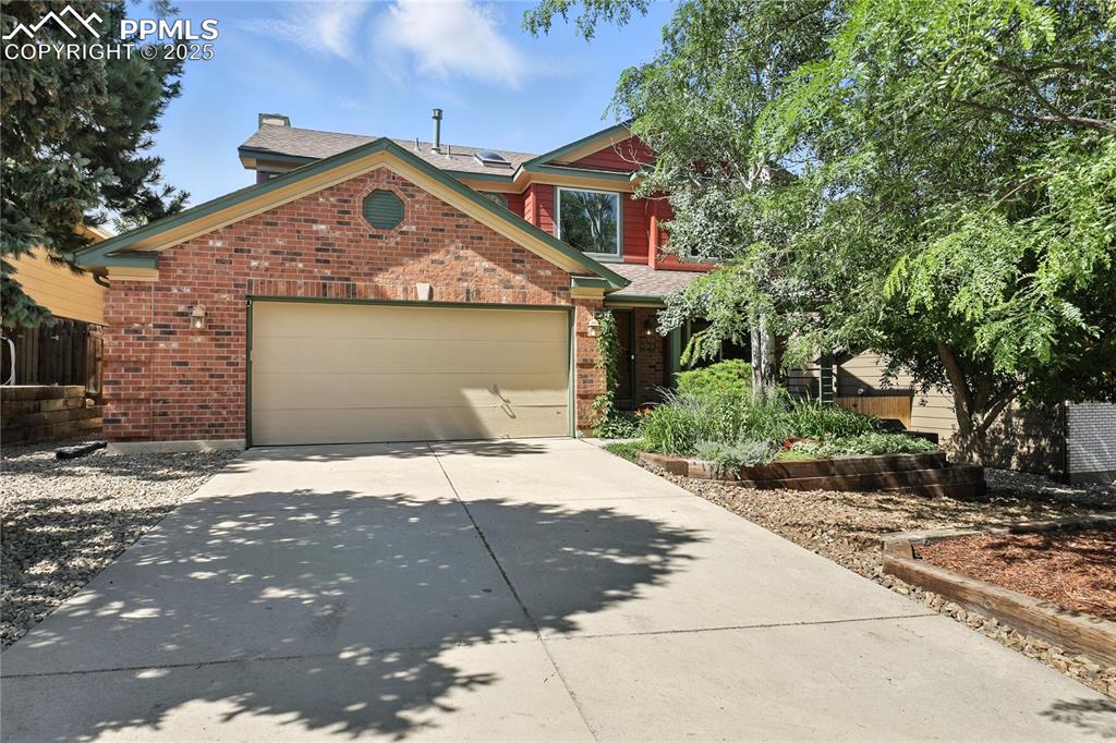 Caption: View of front of home with driveway, an attached garage, brick siding, and roof mounted solar panels