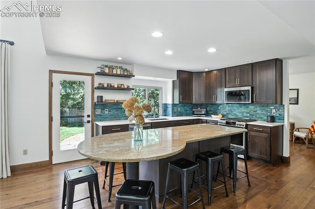 Image 12 of 50: Kitchen with stainless steel appliances, dark brown cabinets, open shelves,