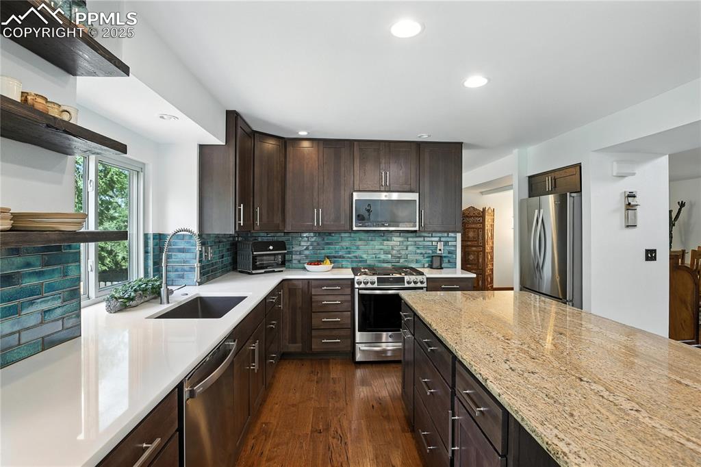 Image 13 of 50: Kitchen with appliances with stainless steel finishes, open shelves, dark b