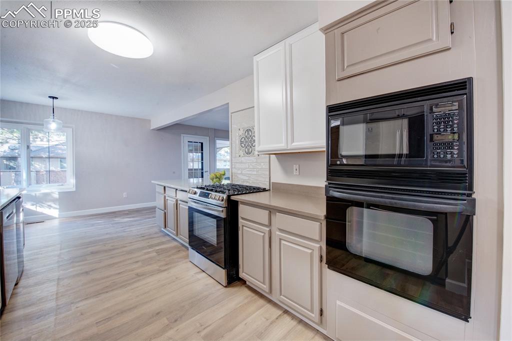 Image 14 of 36: Kitchen with black appliances, light wood-style flooring, light countertops