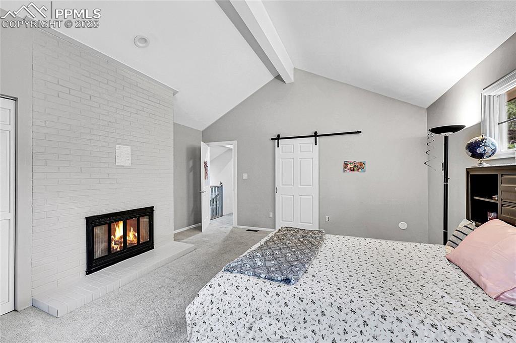 Image 22 of 36: Bedroom featuring a barn door, carpet flooring, and a brick fireplace