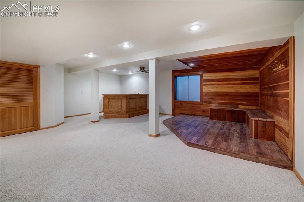 Image 29 of 36: Finished below grade area featuring wooden walls, bar, light carpet, and re