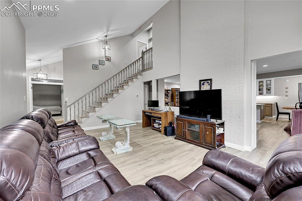 Image 9 of 36: Living area with high vaulted ceiling, wood finished floors, and stairs