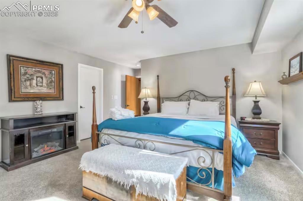 Image 13 of 48: Carpeted bedroom featuring a ceiling fan and a glass covered fireplace