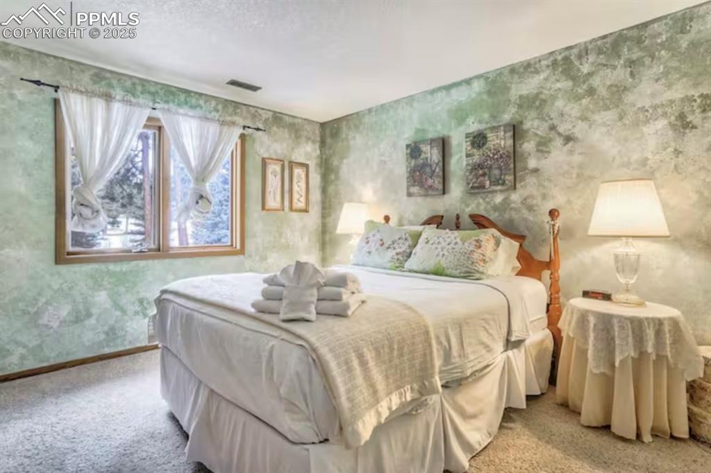 Image 31 of 48: Bedroom with wallpapered walls, carpet flooring, and a textured ceiling