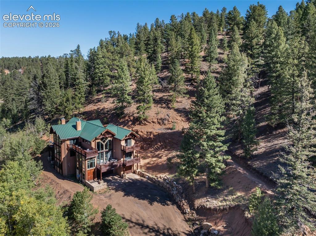 Caption: Multi-story residence featuring a green metal roof, multiple balconies, a stone retaining wall, and 