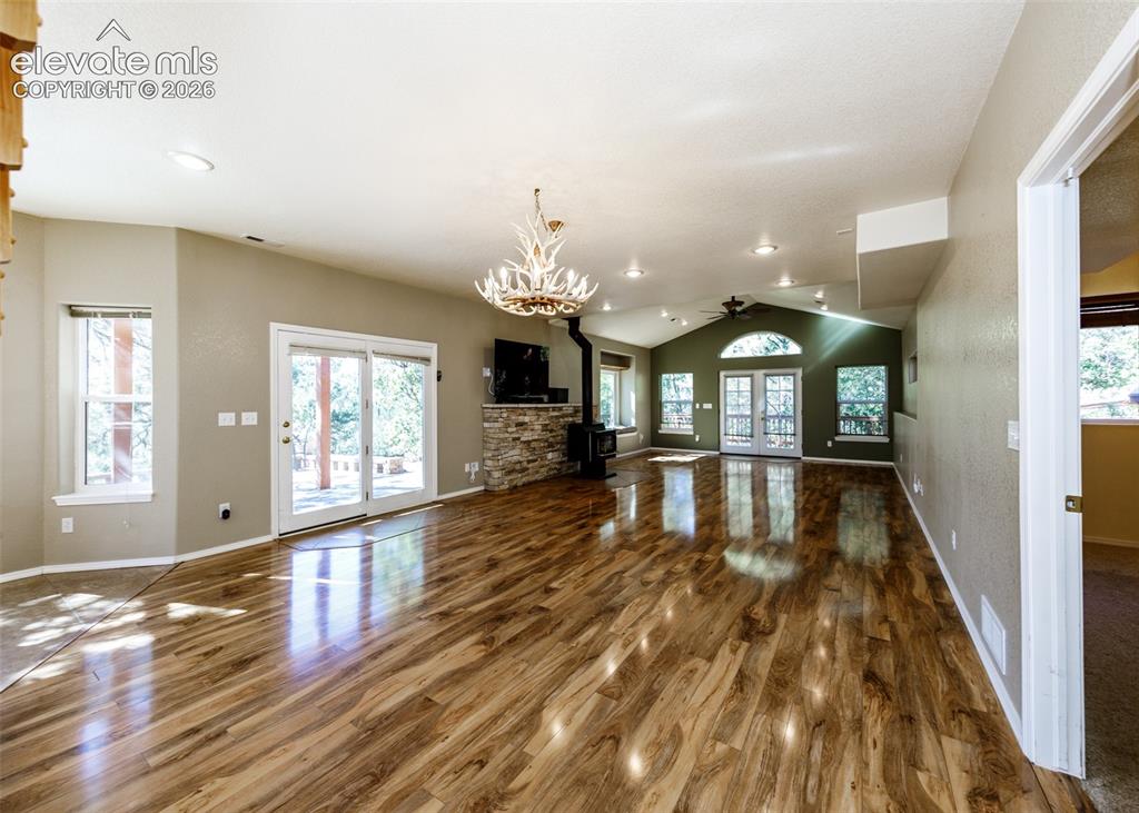 Image 33 of 48: Living area featuring wood-finish flooring, stone-faced fireplace, vaulted 