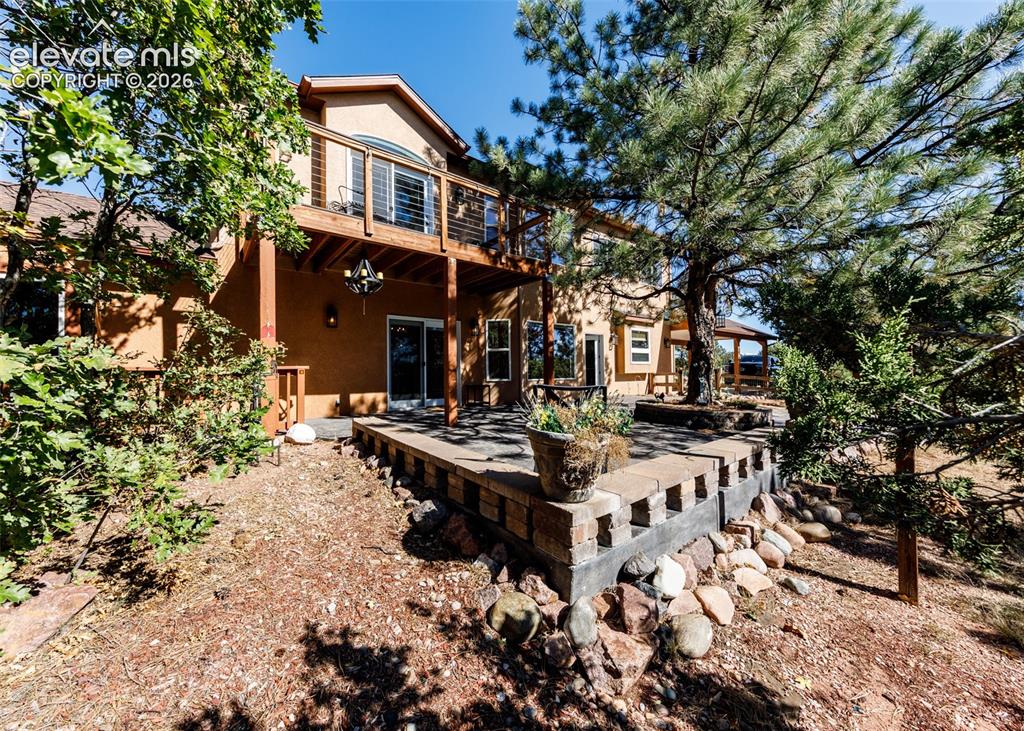 Image 43 of 48: Stucco exterior featuring an elevated wood deck with metal railing, a stone