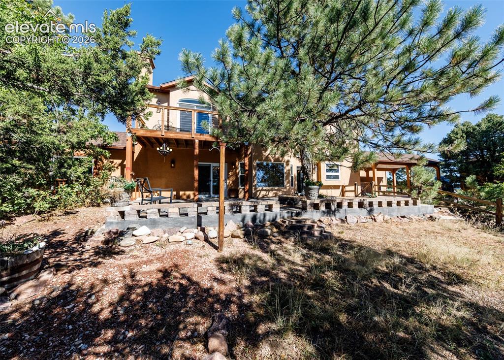 Image 44 of 48: Stucco exterior featuring a raised wooden deck, stone-block retaining wall,