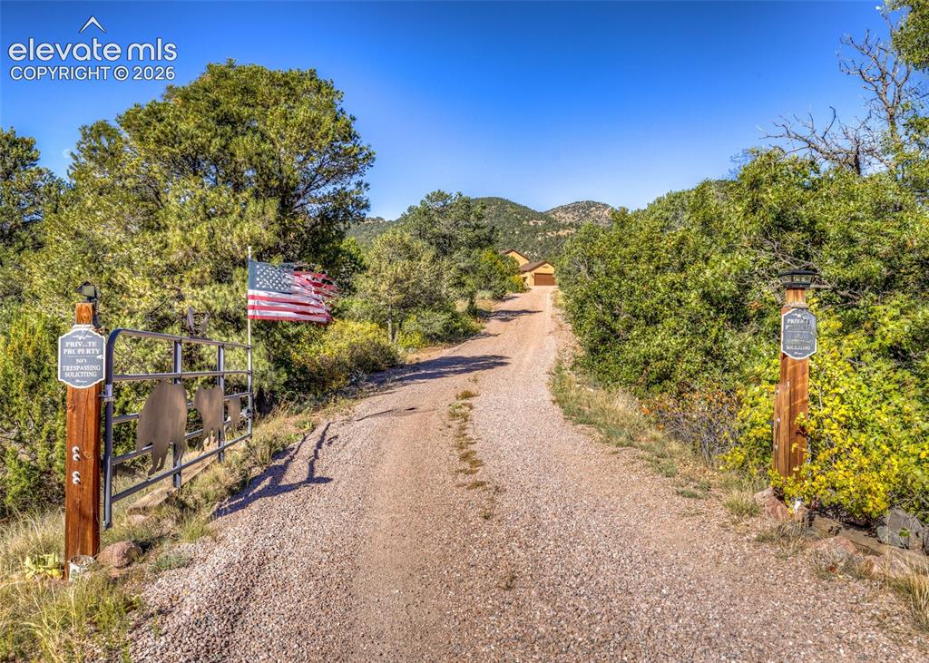 Image 5 of 48: Gravel driveway featuring a decorative metal gate with wood-post supports, 