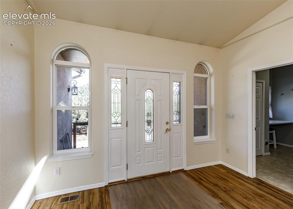 Image 8 of 48: Entryway featuring wood-finish flooring, vaulted ceilings, and a paneled fr