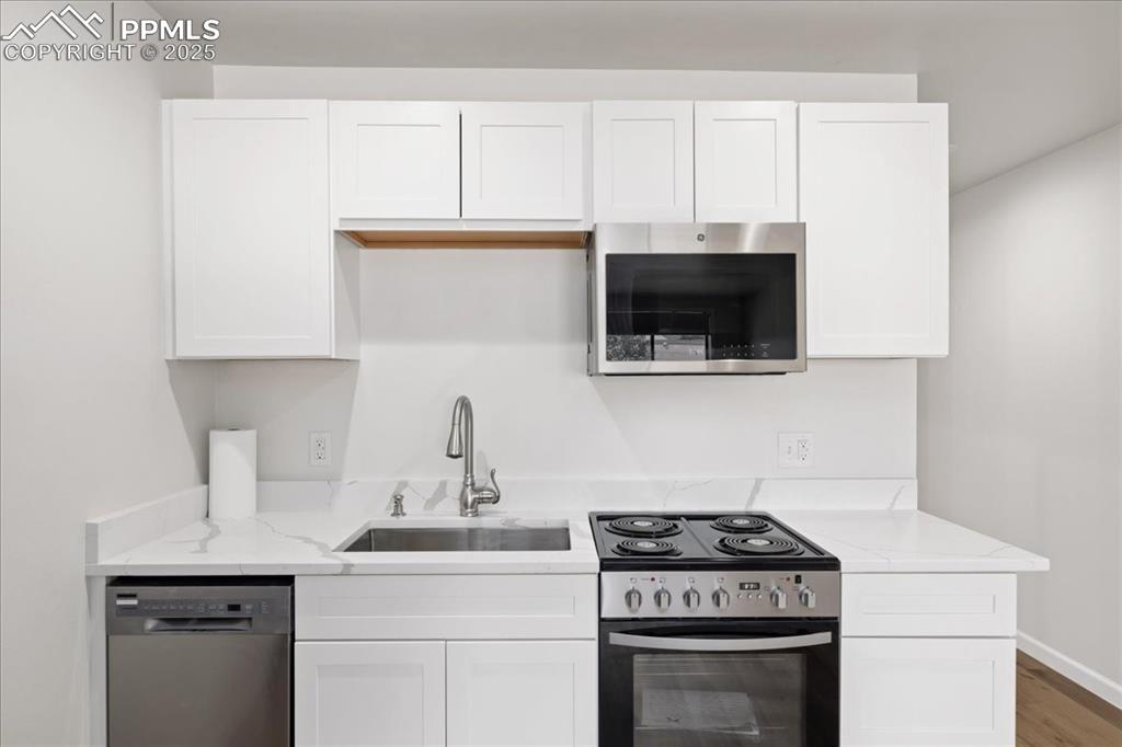 Image 5 of 17: Kitchen featuring stainless steel appliances, white cabinetry, light stone