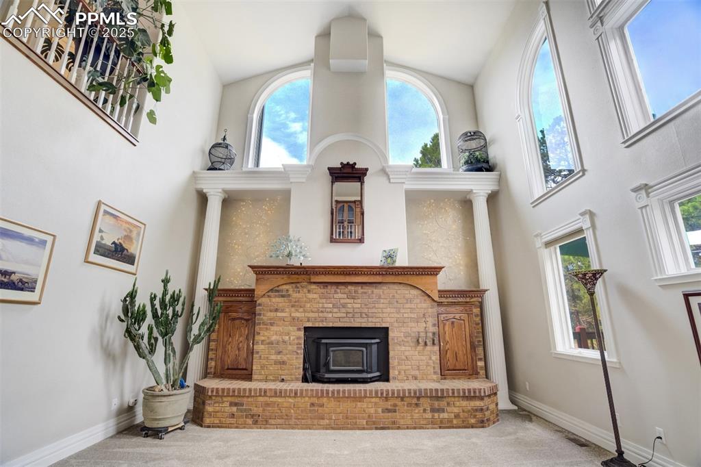 Image 18 of 50: Living room featuring high vaulted ceiling, carpet flooring, wood-burning s