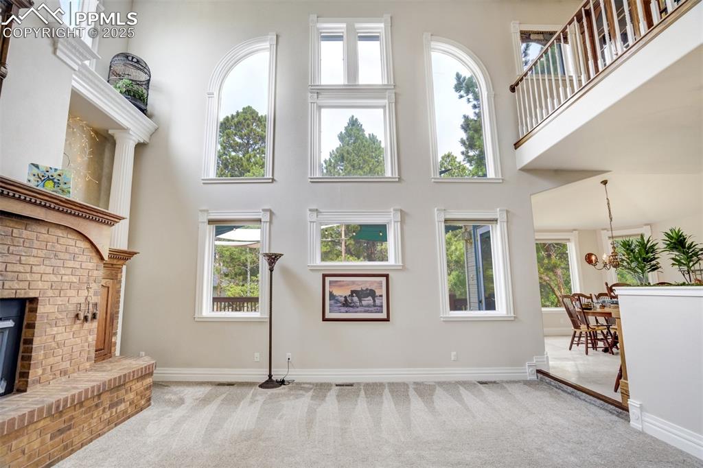Image 19 of 50: Unfurnished living room featuring a high ceiling, carpet flooring, a brick 