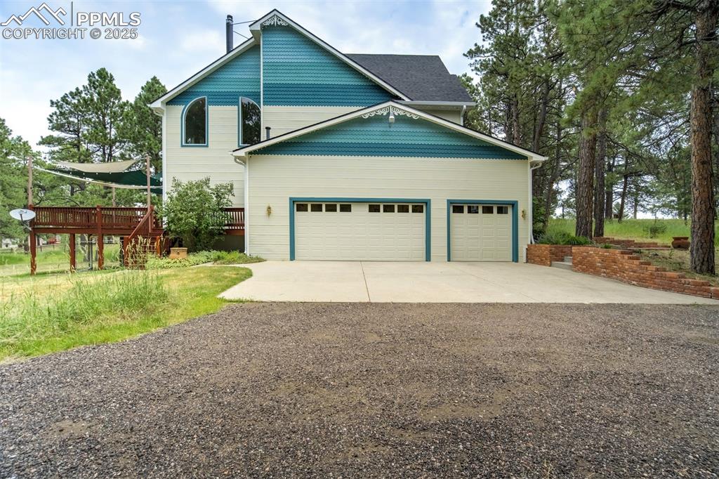 Image 2 of 50: View of exterior with driveway, a wooden deck, and a garage