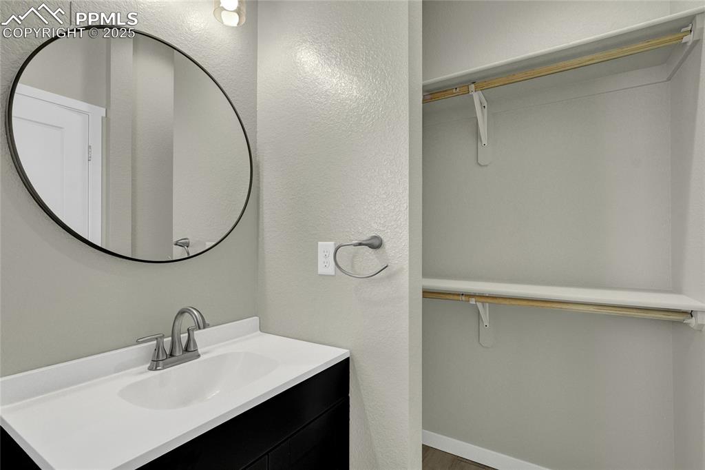 Image 18 of 38: Bathroom featuring a textured wall, vanity, and a walk in closet