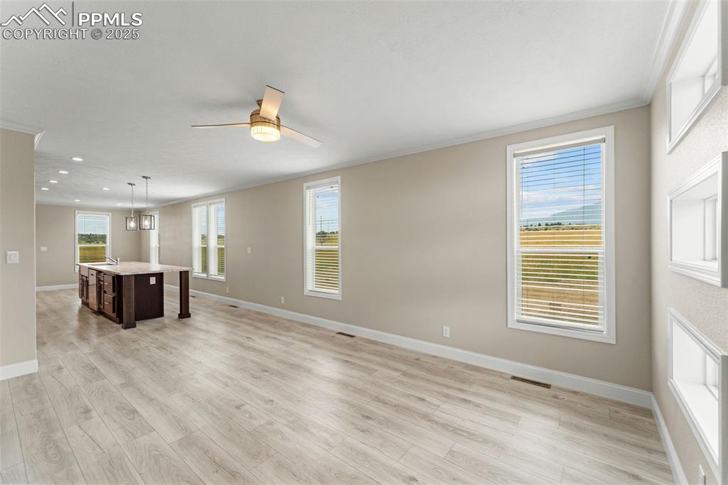 Image 10 of 44: Unfurnished living room with ornamental molding, a ceiling fan, light wood-