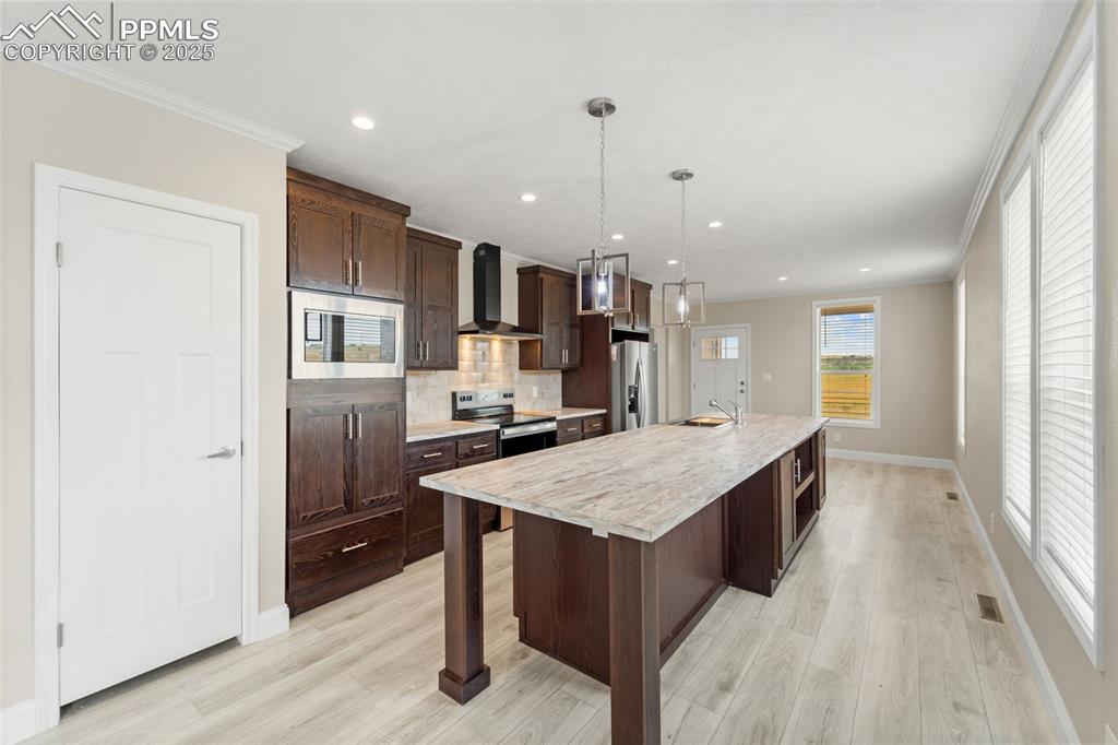 Image 15 of 44: Kitchen with stainless steel appliances, wall chimney exhaust hood, light c