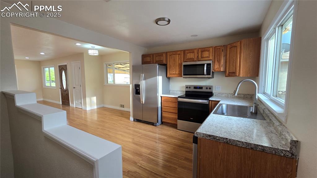 Image 9 of 42: Kitchen with stainless steel appliances, a sink, brown cabinets, light wood