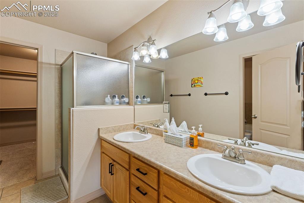 Image 12 of 27: Bathroom featuring a stall shower, double vanity, a spacious closet, and li