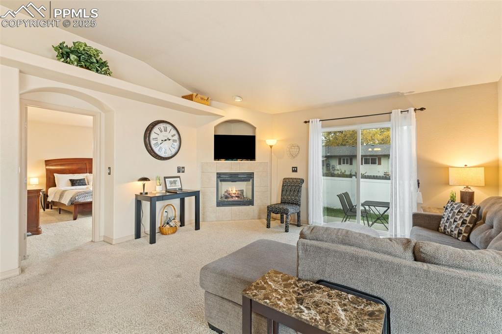 Image 4 of 27: Carpeted living room with a tiled fireplace and lofted ceiling