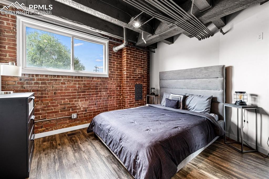 Image 22 of 32: Bedroom featuring brick wall and wood finished floors
