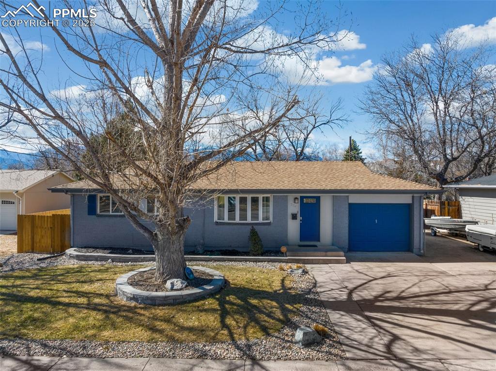 Caption: Ranch-style house featuring concrete driveway, roof with shingles, brick siding, and a garage