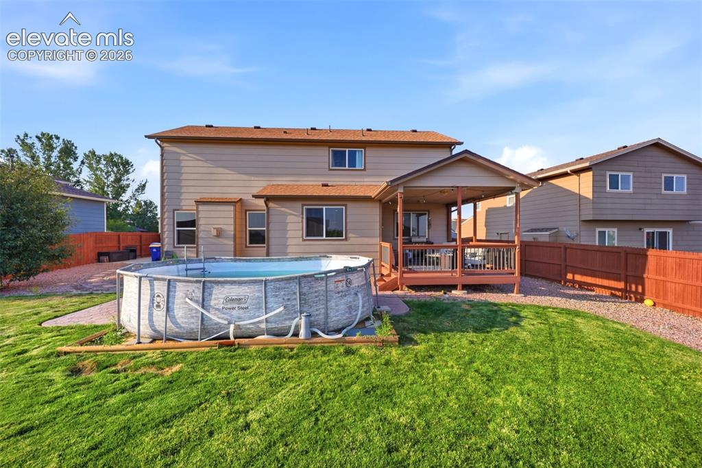 Image 32 of 40: Expansive backyard with a covered deck, vibrant green lawn, and a privacy f