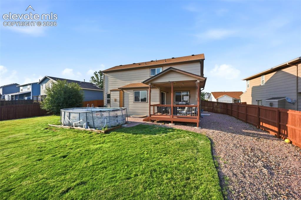Image 33 of 40: Expansive lawn area, covered patio with wood decking, gravel pathway, and p